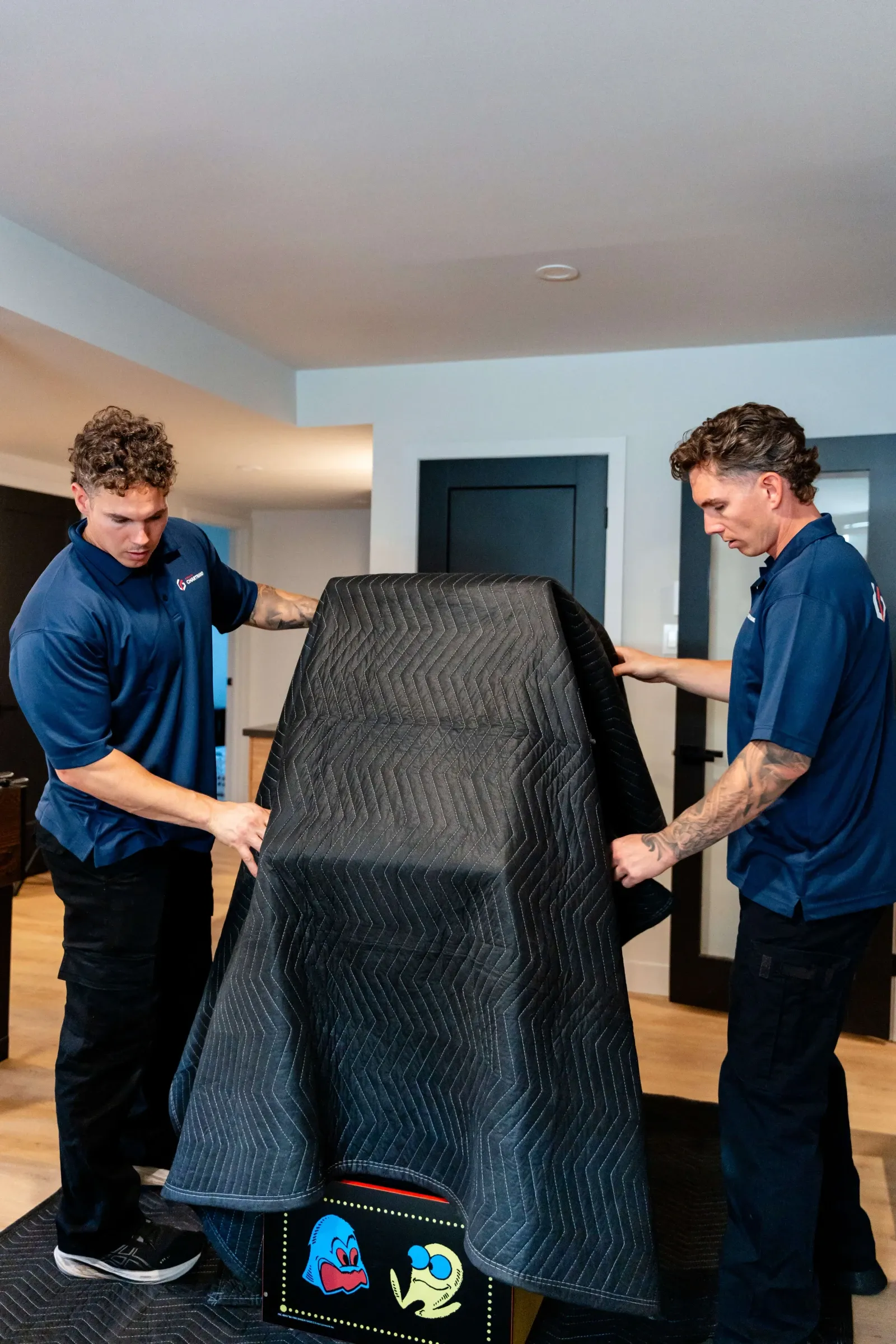 Two Chartrand movers covering an arcade machine with a protective blanket