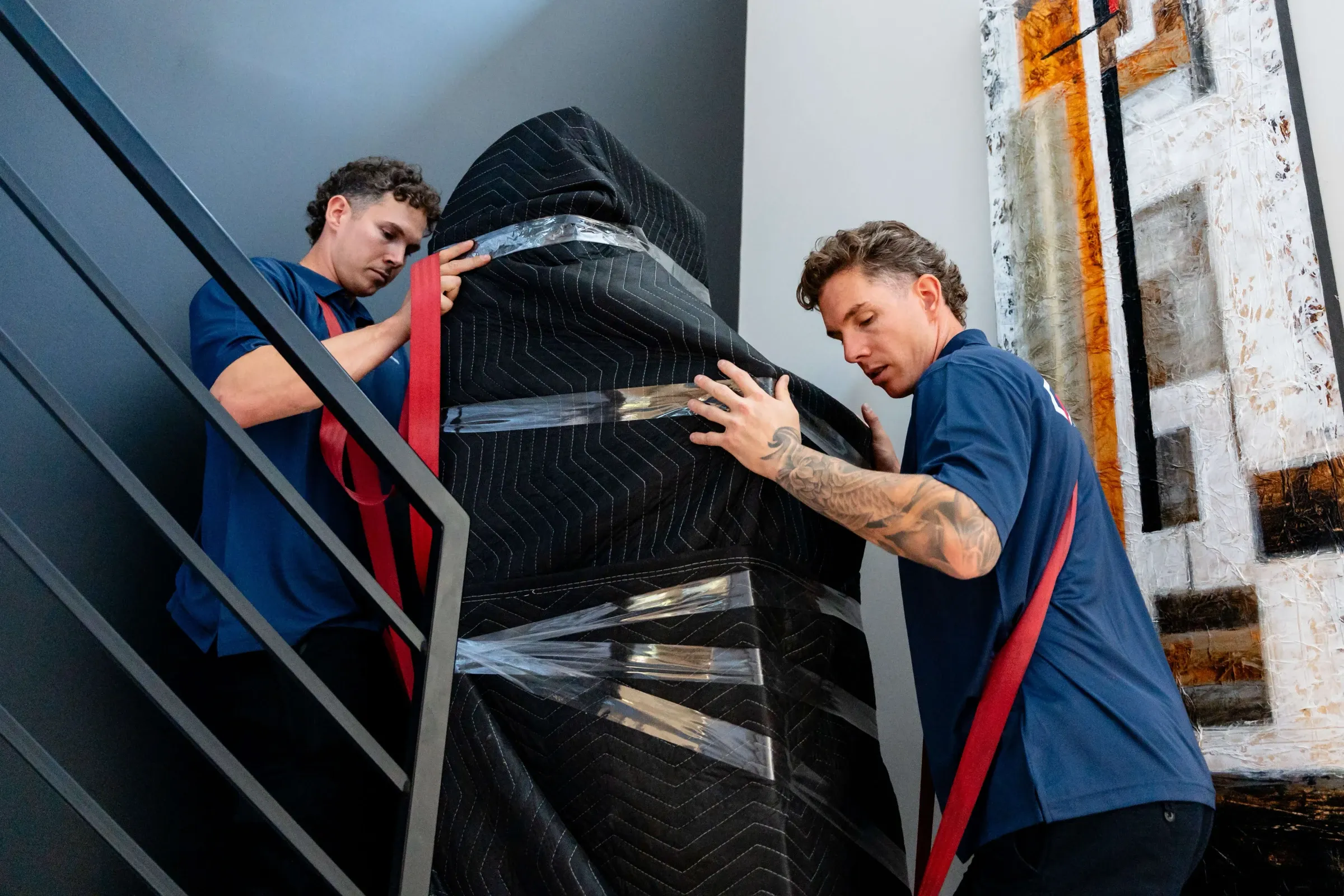 Two Chartrand movers carrying a piece of furniture wrapped in protective blankets up a staircase