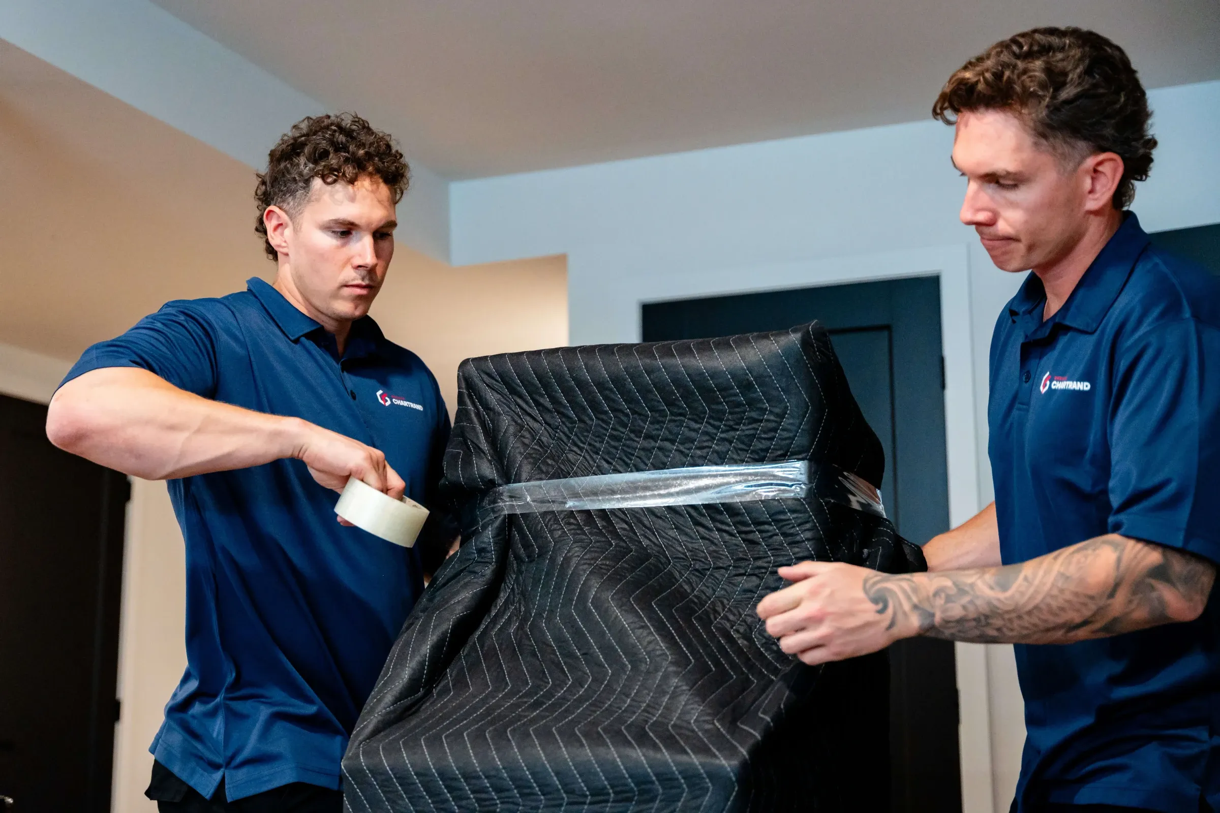Two Chartrand movers taping the protective cover on an arcade machine