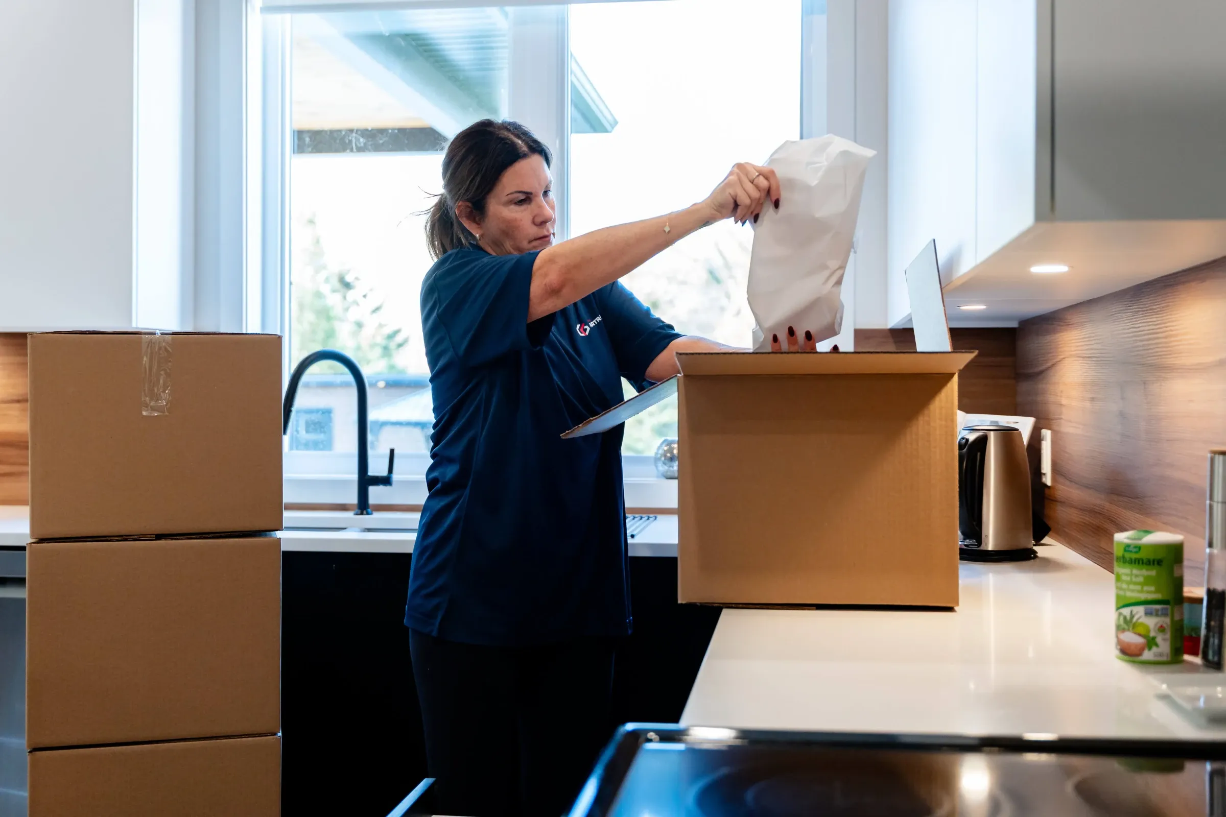 Chartrand packer placing a wrapped item in a box, in a kitchen