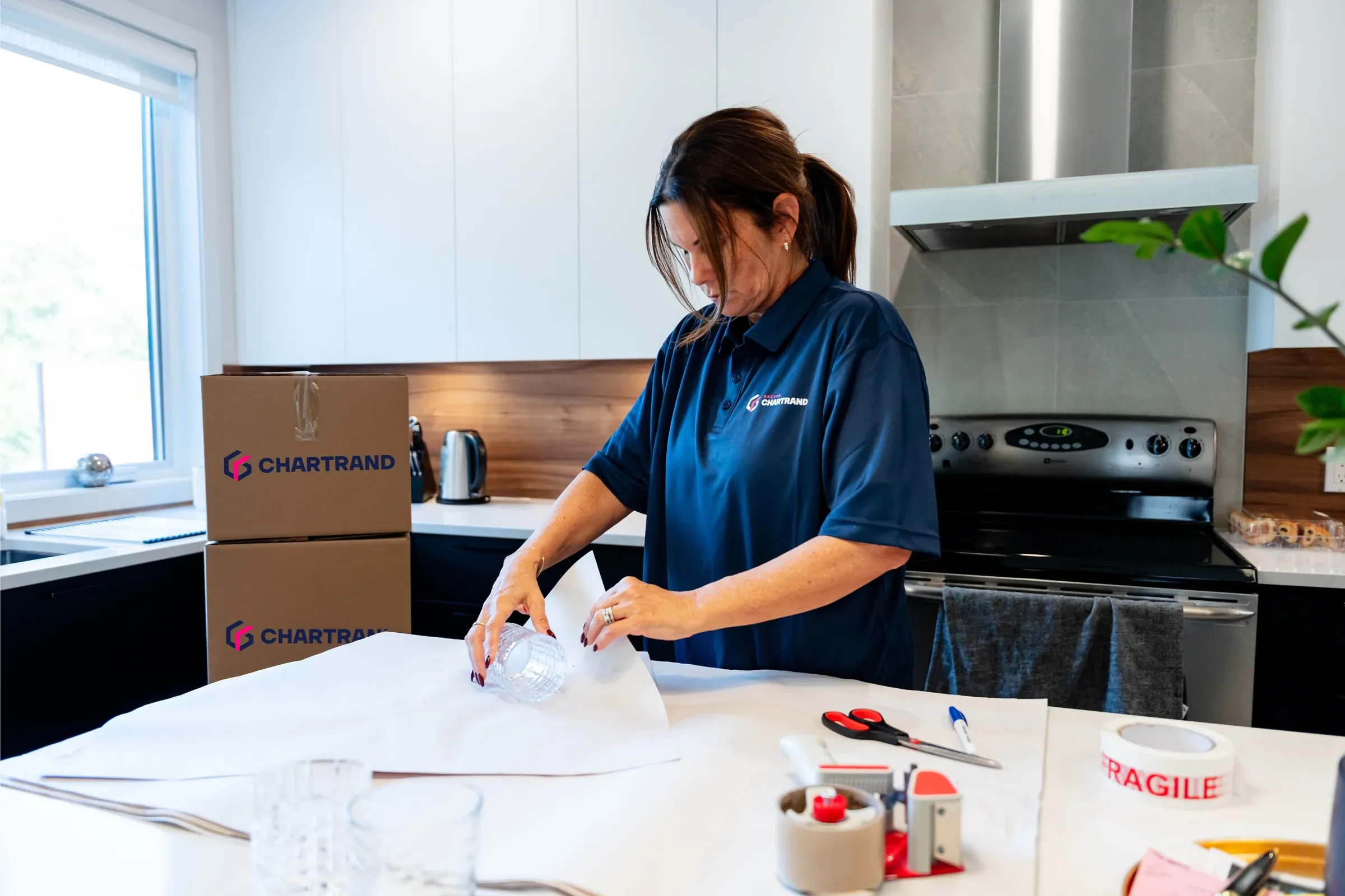 Chartrand packer wrapping a glass in paper, Chartrand boxes behind her